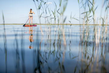 Woman paddleboarding on the lake with reeds and calm water during the morning light