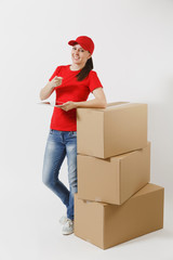 Full length portrait of delivery young woman in red cap, t-shirt isolated on white background. Female courier standing near empty cardboard boxes with tablet pc computer. Receiving package. Copy space