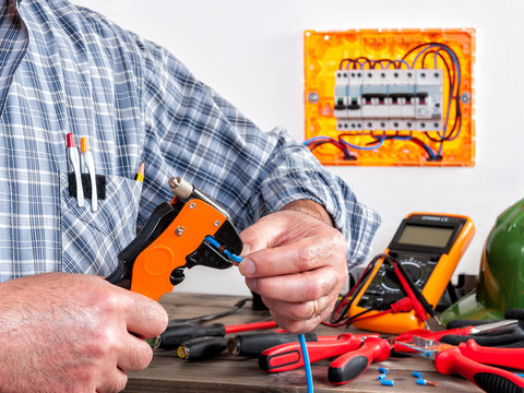 Electrician at work on cables with wire stripper.