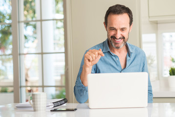 Middle age man using laptop at home pointing with hand and finger up with happy face smiling