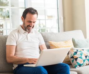 Middle age man using laptop at sofa with a happy face standing and smiling with a confident smile...