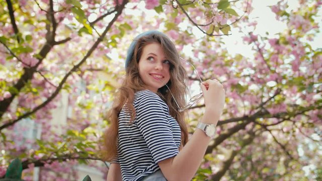 Young beautiful happy smiling lady wearing beret and striped shirt posing under the blooming sakura