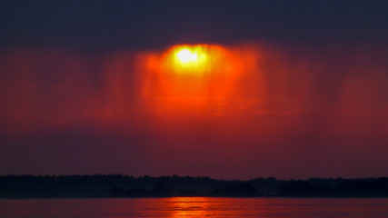 Red sunset and dark rainy clouds reflected in calm water.