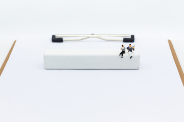 Miniature businessman sitting on white block, it can write for various occasions. Image use for business background concept.