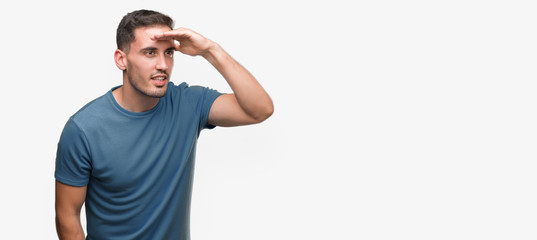 Handsome young casual man very happy and smiling looking far away with hand over head. Searching concept.