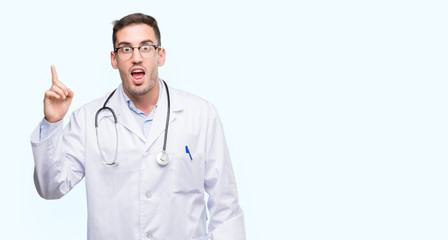 Fototapeta premium Handsome young doctor man pointing finger up with successful idea. Exited and happy. Number one.