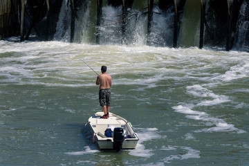 Een man in een boot die bij de dam aan het vissen is