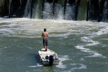 Abwaschbare Fototapete Wasser Motorsport Ein Mann in einem Boot, das in der Nähe des Damms fischt