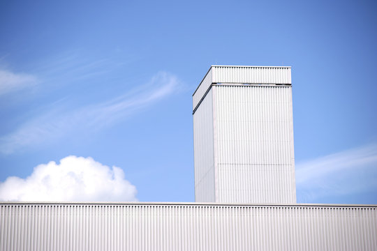 Dachkante Industriehalle / Die Dachkante einer Industriehalle aus Wellblech vor einem blauen Himmel mit Wolken.
