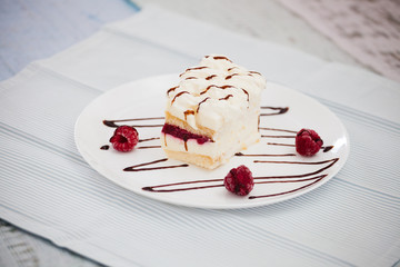 Dessert of cake and raspberries on a large white plate on a napkin in blue stripes