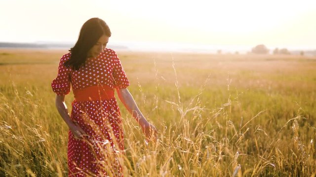 Beautiful young girl walking on field with wildflowers, enjoying nature outdoors Slow motion video. girl in the field at sunset in a red dress hand close-up on the grass sunlight silhouette lifestyle