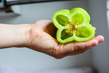 Cut fresh green peppers with seeds in a woman's hand before preparing lunch in the kitchen. Organic food. Shallow depth of field.