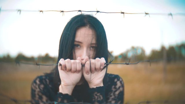 girl brunette refugee behind barbed wire camp slow motion video. the concept of freedom is upset Woman hands and lifestyle barbed wire. girl Refugee, prison, refugees captivity concept