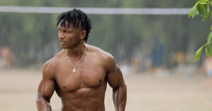 Sexy macho man with muscular body running on beach under rain