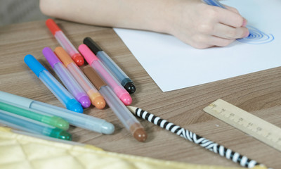 Close-up of the child's hands draw ovals with a blue marker on white paper