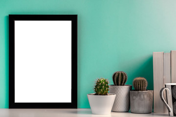 Blank black frame with cactuses, books and a black mug with coffee on the background of a bright mint wall - Powered by Adobe