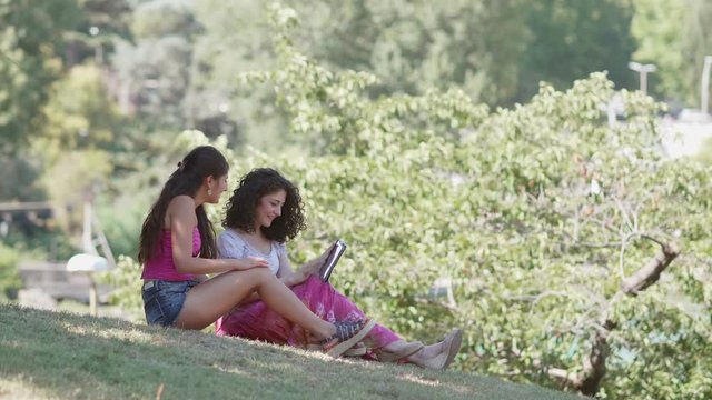 Relaxed happy girlfriends using tablet in the park