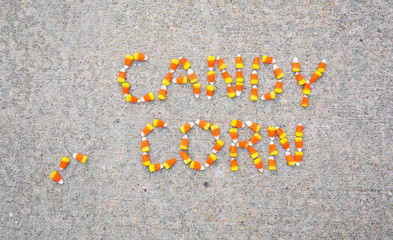 The words Candy Corn spelled out with candy corn on a sidewalk with three extra candy corns beside the words.