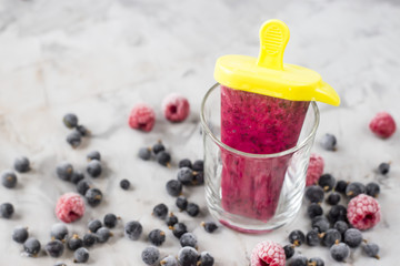 Berry ice cream on a stick in transparent glasses. Homemade of raspberries and currants, cooked with special forms. On a gray table among frozen berries