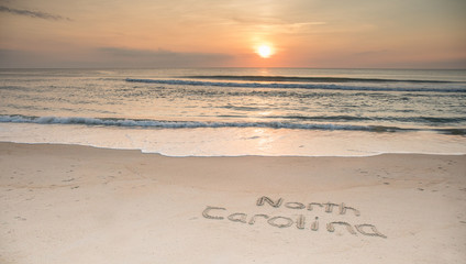 Fototapeta na wymiar The words North Carolina etched in the sand at sunrise with waves coming ashore.