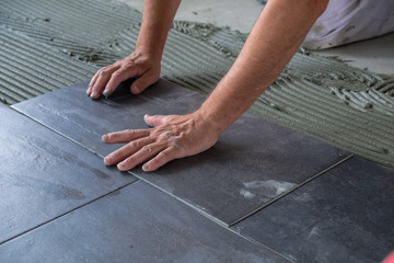 Worker placing ceramic floor tiles on adhesive surface. Manual labor and craftsmanship background.