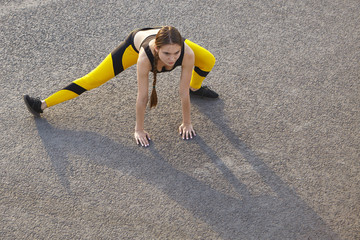 Beautiful young woman jogger in sportswear doing side lunges, stretching legs muscles after running workout, casting shadow on asphalt. People, sports, flexibility, strength and endurance concept