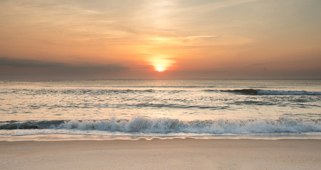 Fototapeta na wymiar The sun rising over the ocean at sunrise with waves crashing ashore.