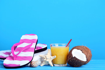 Flip flops with coconuts and glass of juice on blue background