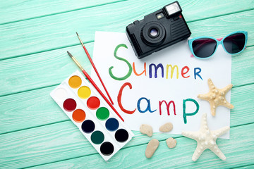 Inscription Summer Camp with retro camera and starfishes on wooden table