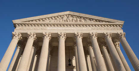 Looking up at the US Supreme Court building in Washington, DC with a bright blue sky.