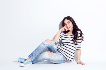 Beautiful woman in jeans and sweater sitting on white background