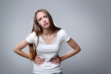 Young woman having stomach ache on grey background