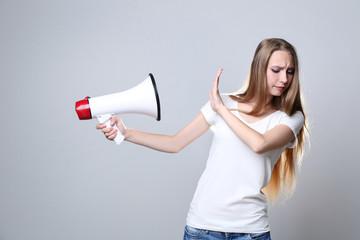 Young woman with megaphone on grey background