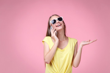 Portrait of young woman in sunglasses and smartphone on pink background