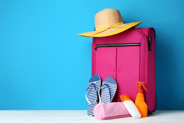 Pink suitcase with flip-flops, hat and sunscreen bottles on wooden table