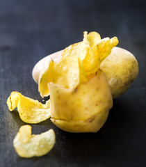 Chips inside potato peel, black wooden background