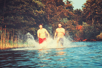 Glückliche junge Menschen laufen und springen am See beim Sonnenuntergang
