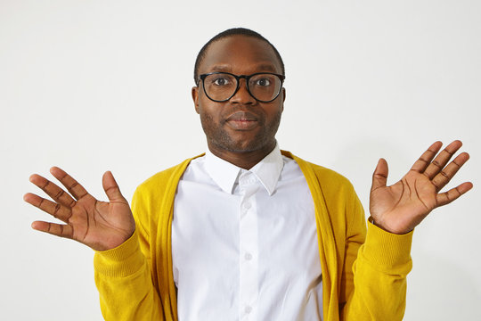 I don' know, who cares, not my problem. Studio portrait of clueless fashionable young African male in spectacles and yellow cardigan, making indifferent or uncertain gesture. Body language