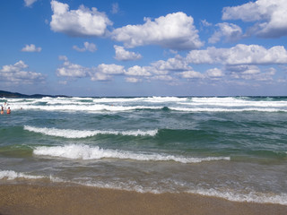 Fototapeta na wymiar Waves meet a sandy Black Sea beach, bathing people in the water distance