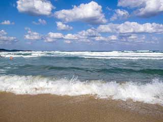 Fototapeta na wymiar Wave meets a sandy Black Sea beach, bathing people in the water distance