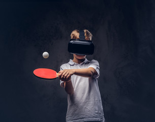 Little redhead boy dressed in a white t-shirt playing ping-pong with a virtual reality glasses....