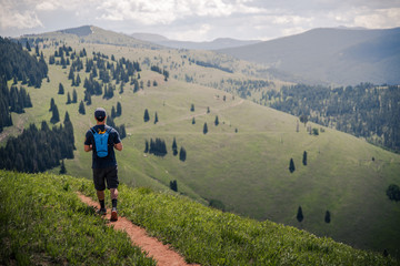 A man hiking on a trail with Vail's back bowls in the background during summer. 