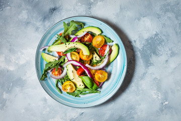 Salad with tomatoes and avocado on concrete background.