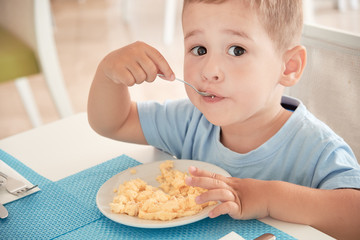 funny boy has Breakfast eggs alone holding a spoon.