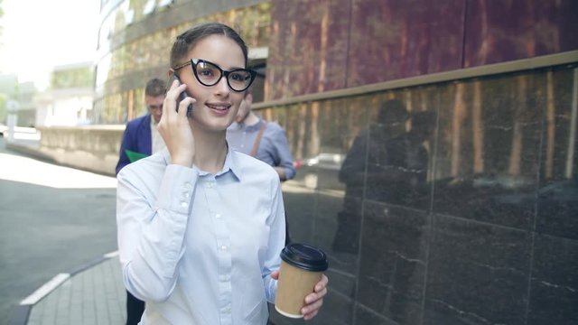 Portrait of confident businesswoman in city talking on phone, beautiful female manager  having mobile conversation while strolling with coffee to go