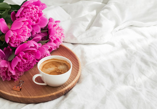 Peonies and coffee on the wooden tray in bed.