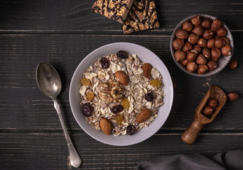 Muesli in white bowl on gray natural desk with nuts and biscuits around.