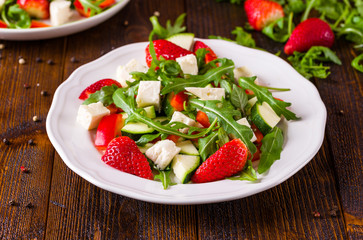 Fresh vegetable strawberry salad on white plate on natural rustic desk.