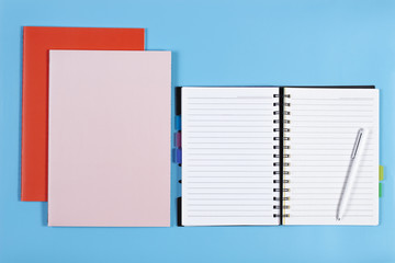 Open notebook with white pen and colorful notebooks on blue background