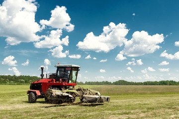 Agricultural machinery, harvester mowing grass in a field against a blue sky. Hay harvesting, grass harvesting. Season harvesting, grass, agricultural land.